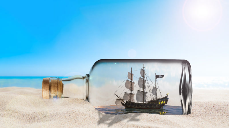 A composition of a ship in a bottle in the sand on the beach.